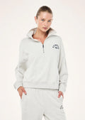Woman wearing a light gray P.E nation tracksuit with a brand logo on a white background