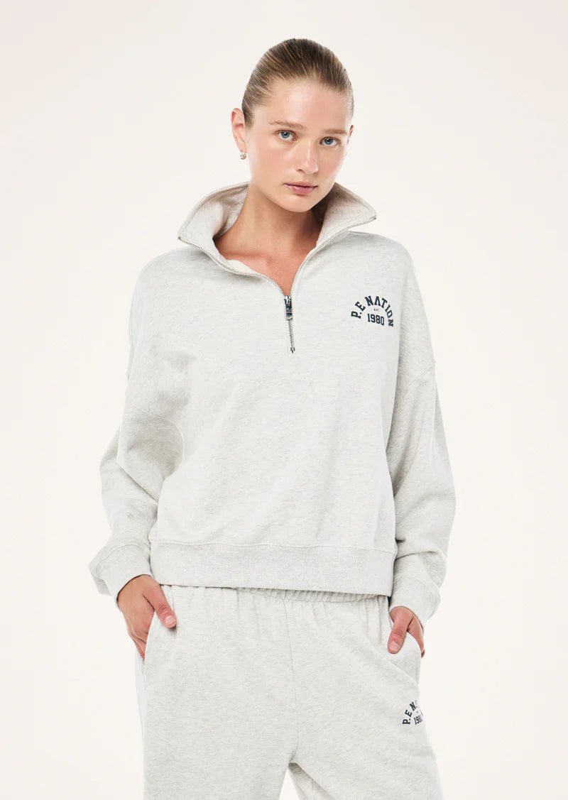 Woman wearing a light gray P.E nation tracksuit with a brand logo on a white background