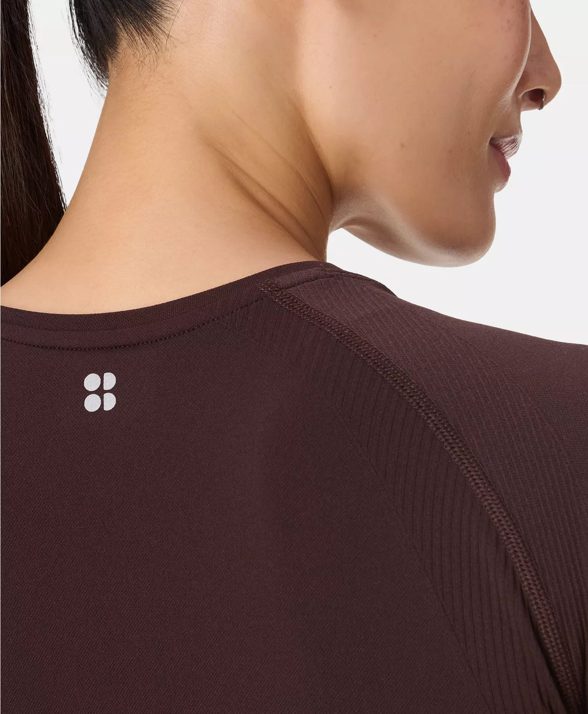 Close-up of a person wearing a dark brown shirt with a logo on the chest.