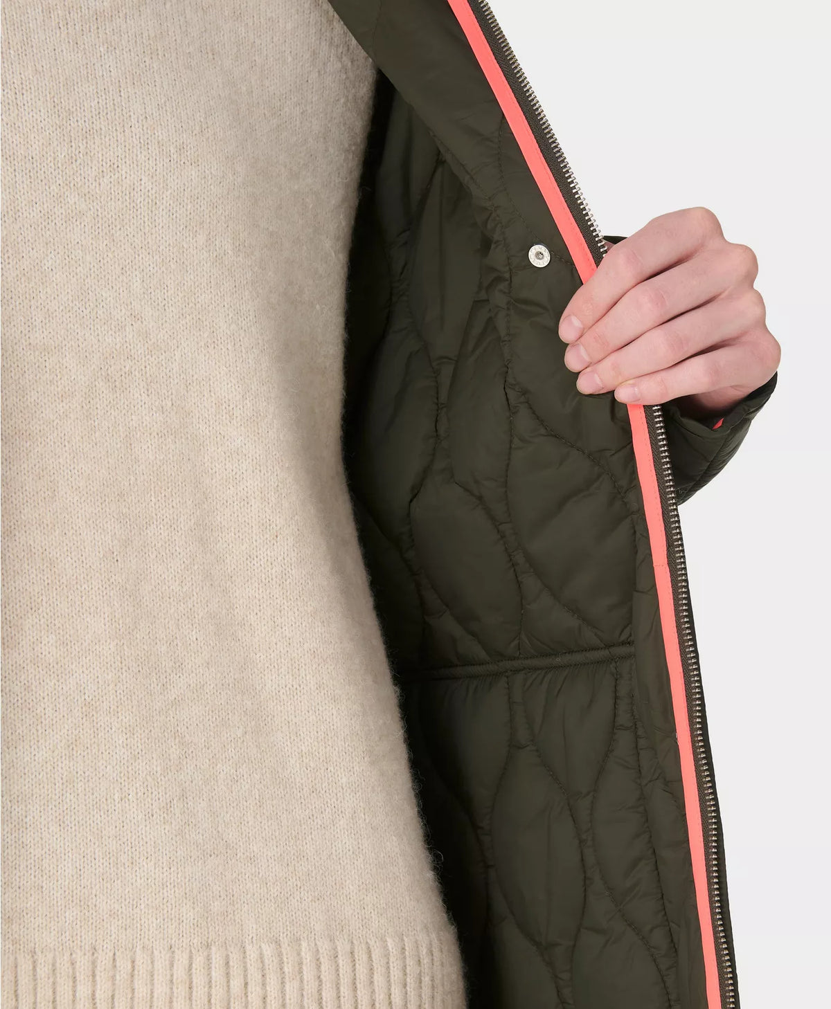 Person wearing a dark green quilted jacket with a pink interior lining, held by a hand.