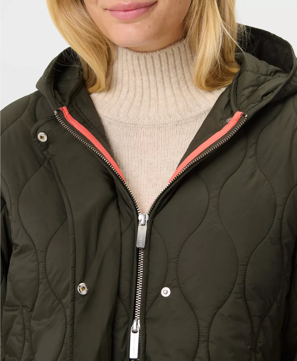 Person wearing a dark quilted jacket with a light-colored sweater underneath on a white background