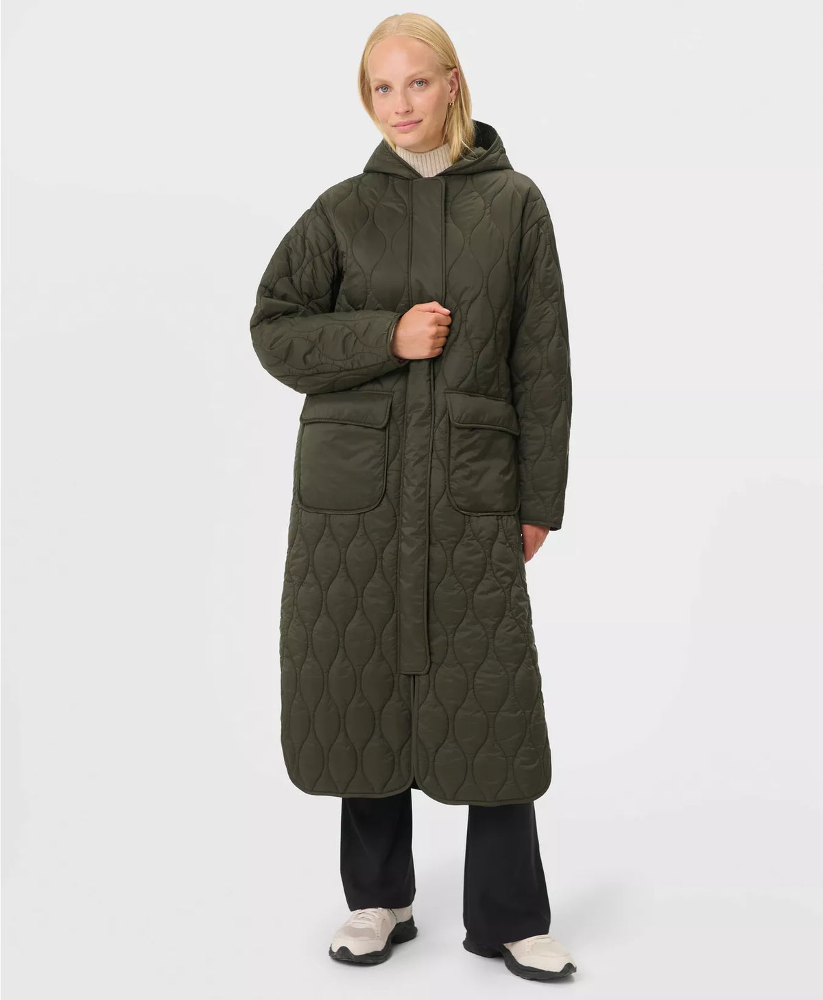 Person wearing a long quilted green coat on a white background