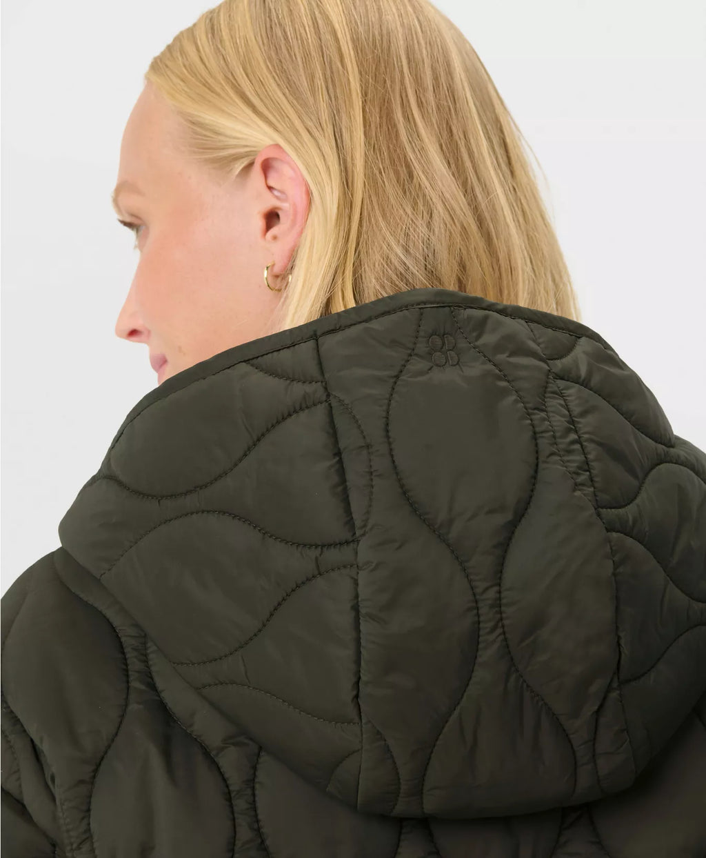 Person wearing a dark green quilted jacket on a plain background