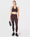 Woman wearing a maroon sports bra and leggings set, holding a black water bottle on a white background