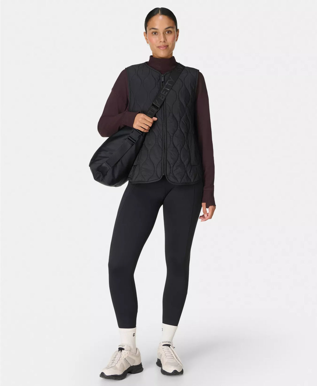 Person wearing a dark quilted vest, black leggings, and white sneakers on a white background