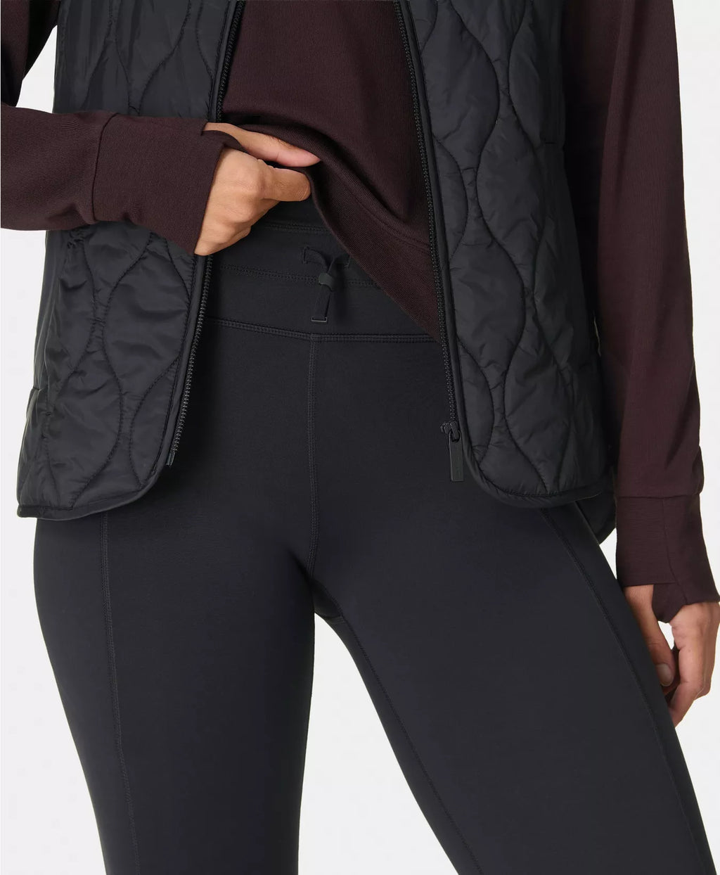 Person wearing a dark quilted jacket and black pants on a white background