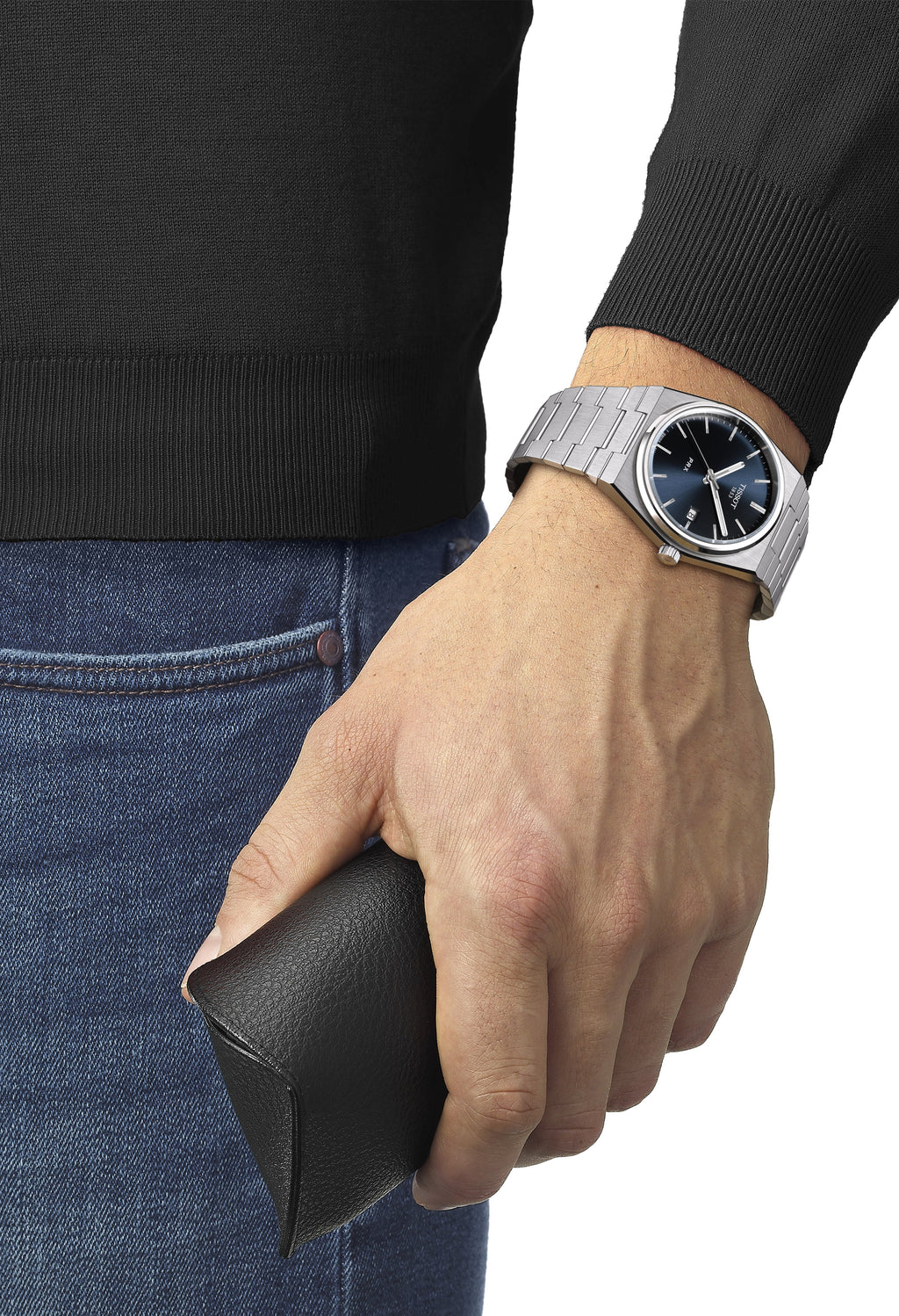 Man wearing Tissot PRX watch with blue dial and stainless steel bracelet, holding sunglasses case, showcasing wrist watch