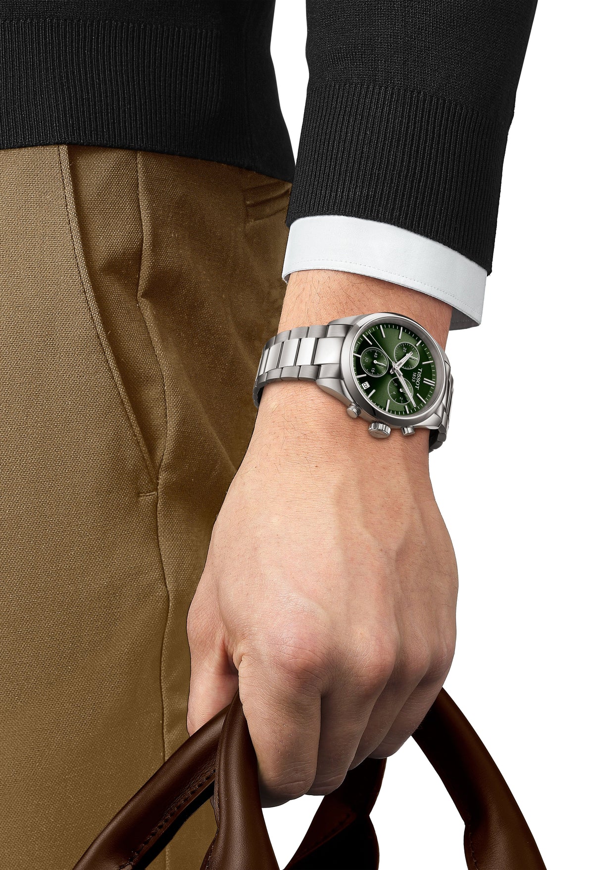 Man showcasing the Tissot PR100 watch with green dial and stainless steel bracelet, holding a bag. Classic style and detail.