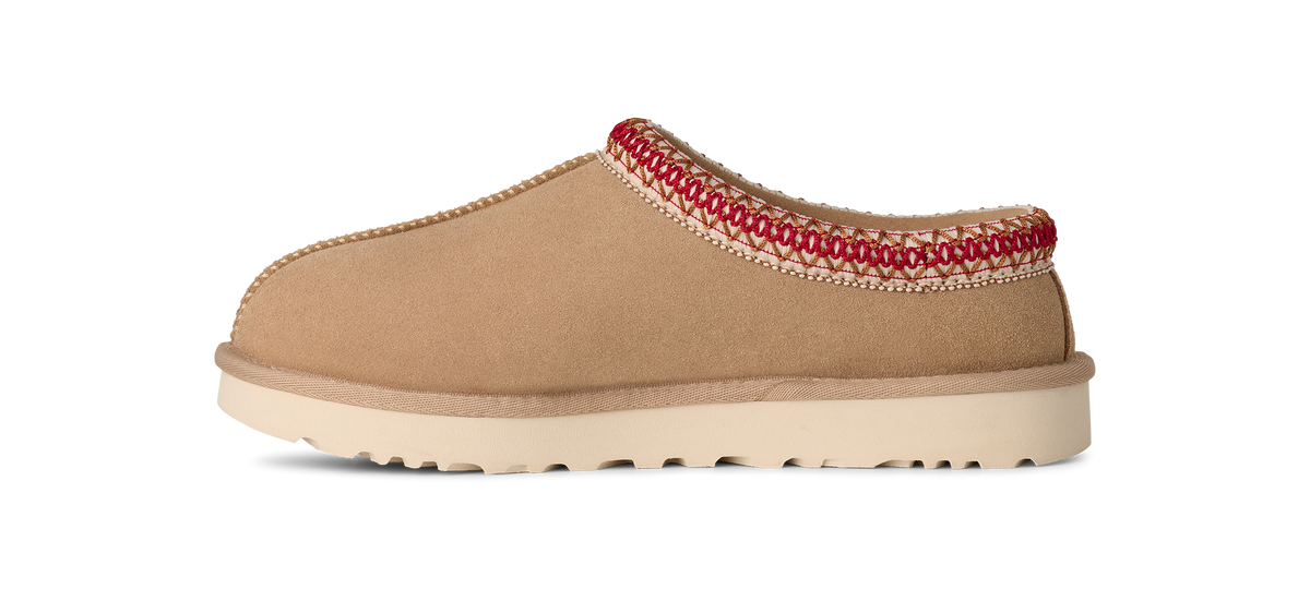 Tan UGG slipper with red trim on a white background
