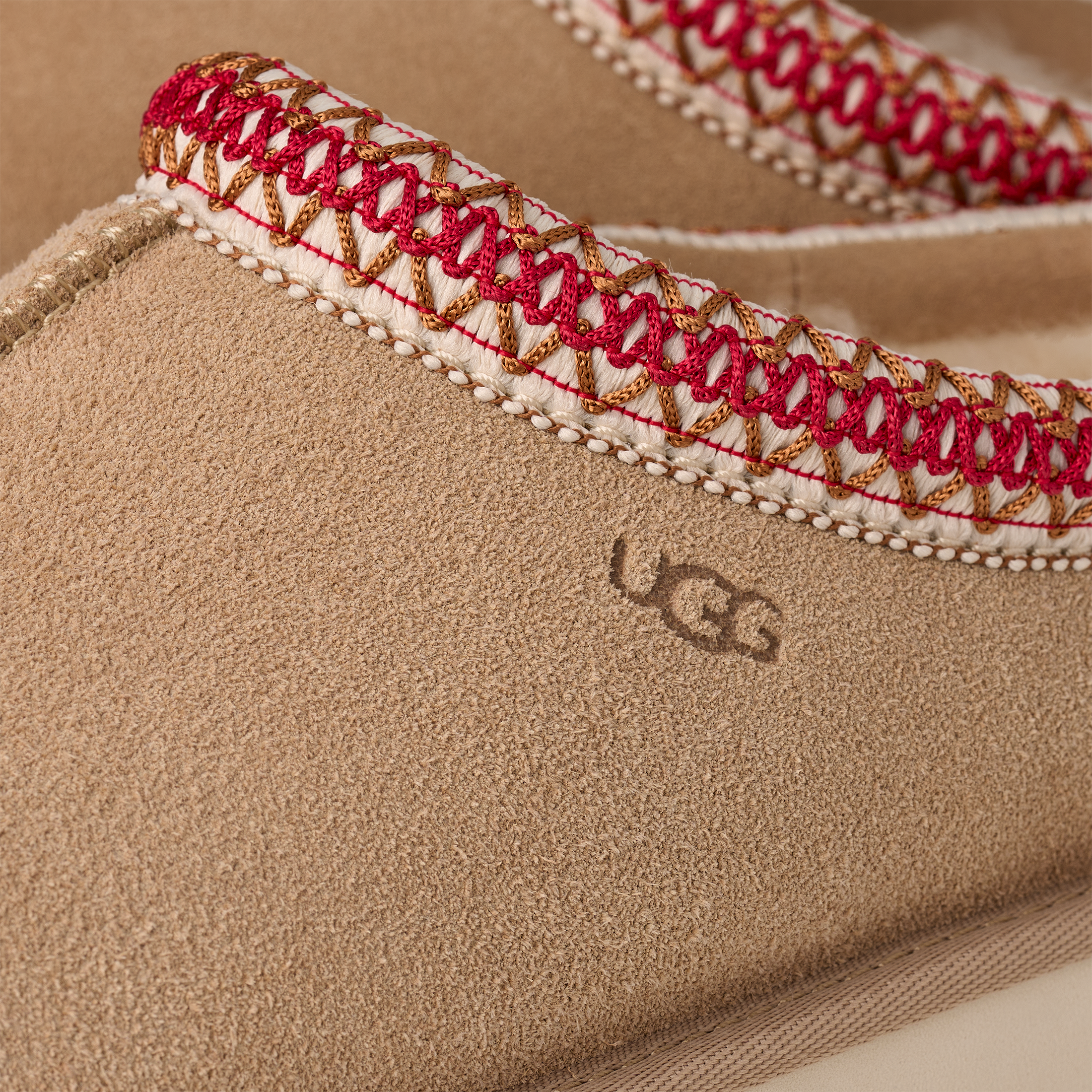 Close-up of a UGG slipper with red and gold embroidery on a beige background