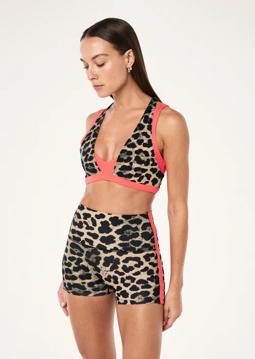 Woman wearing a leopard print sports bra and shorts with pink accents on a white background