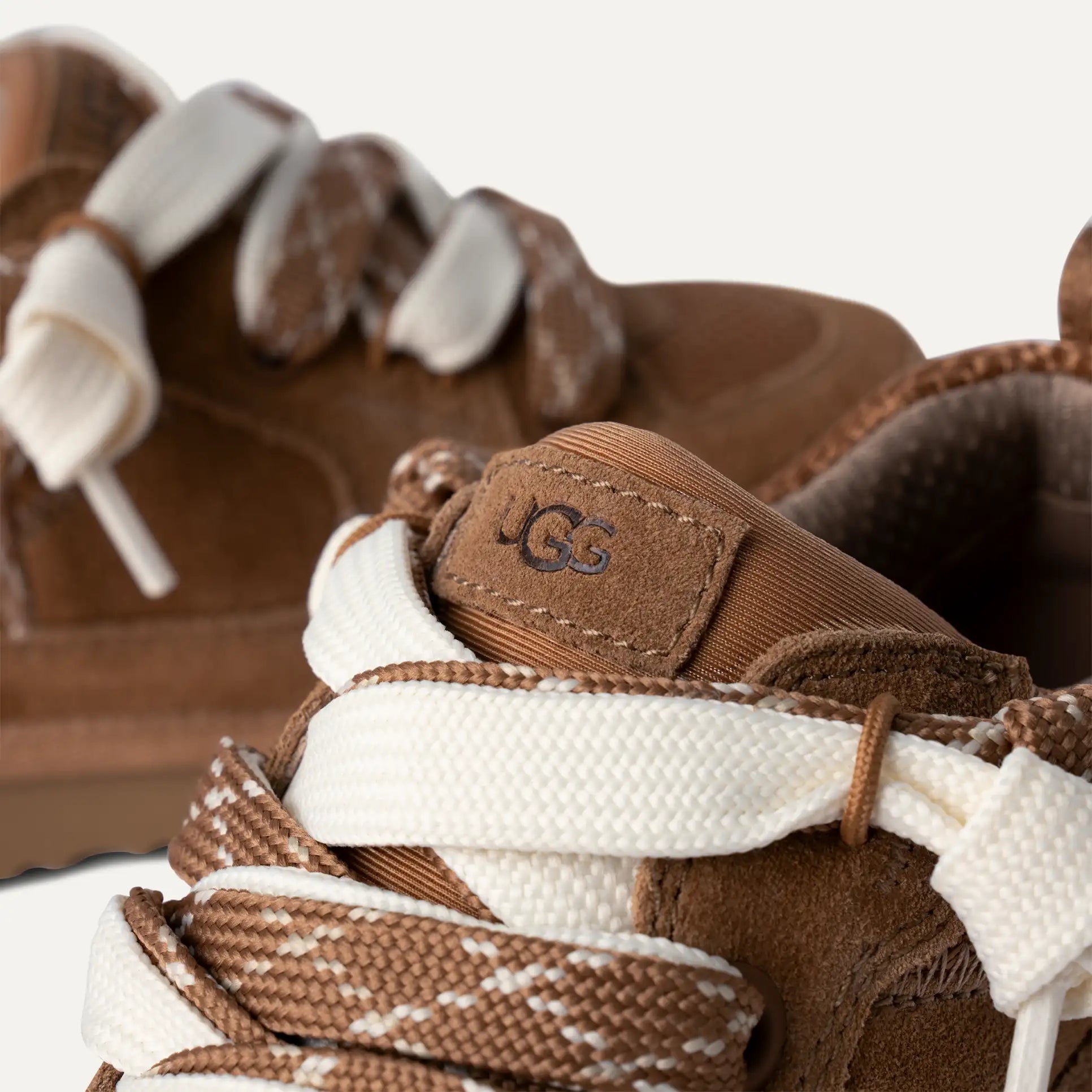 Close-up of brown and white laced shoes with a logo on a white background.