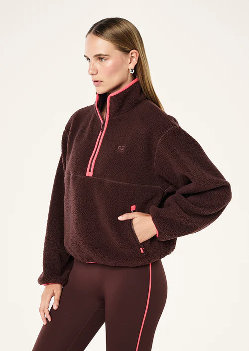 Woman wearing a brown fleece pullover with pink accents on a white background