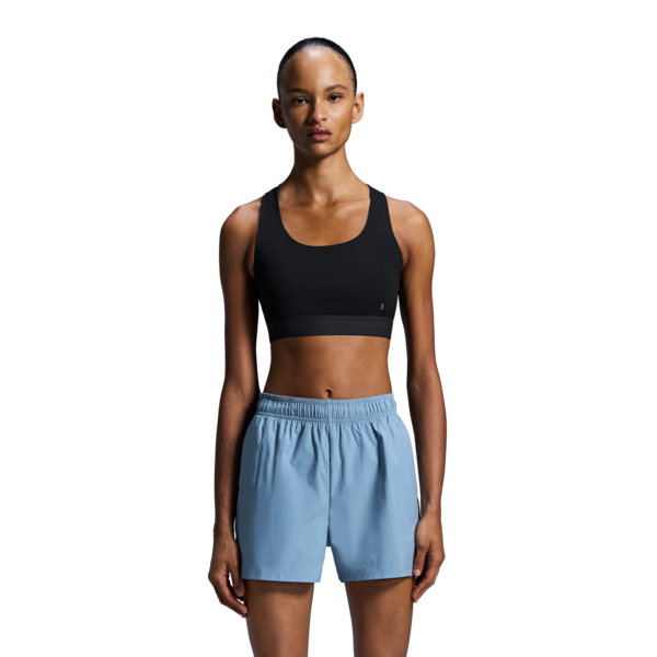 Woman wearing a black sports bra and light blue shorts on a white background