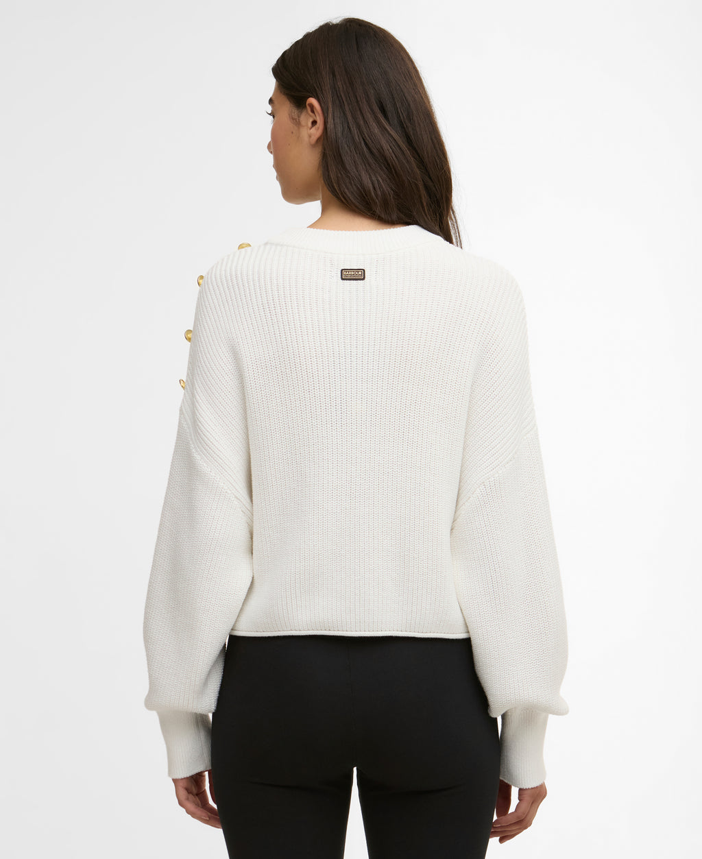 Person wearing a white sweater with yellow buttons on a plain background