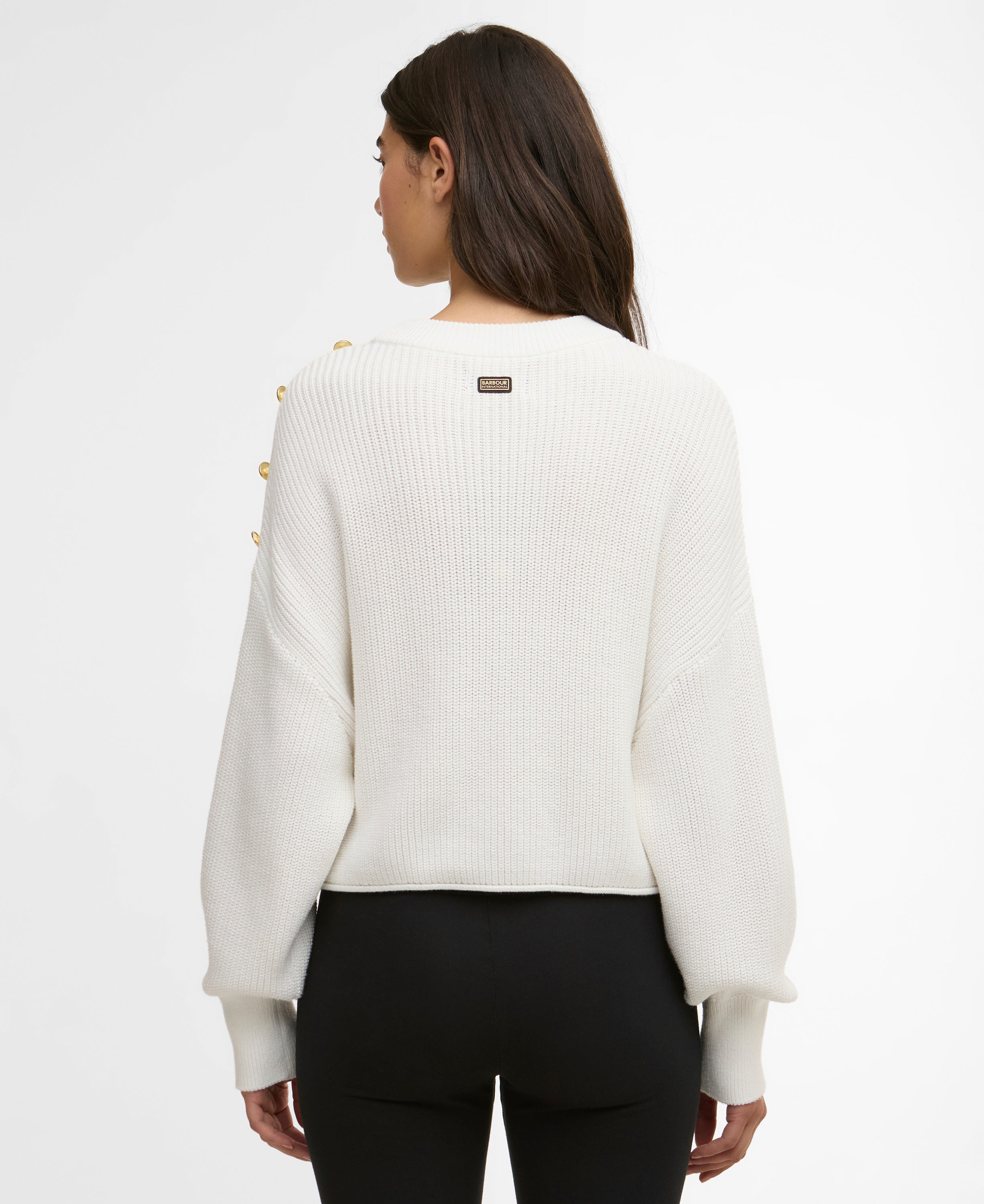 Person wearing a white sweater with yellow buttons on a plain background