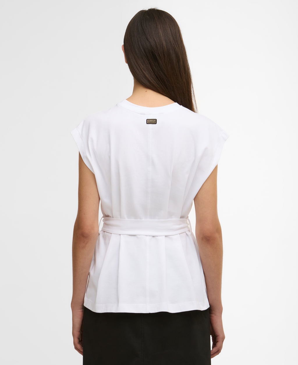 Woman wearing a white top with a belt on a plain background