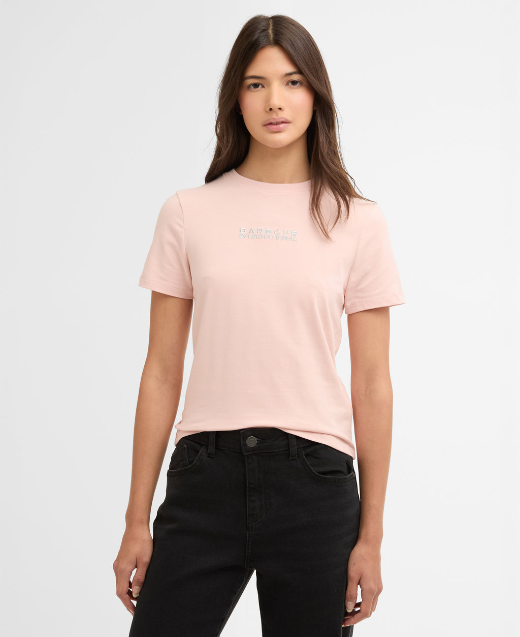 Woman wearing a light pink t-shirt with a barbour logo on a white background
