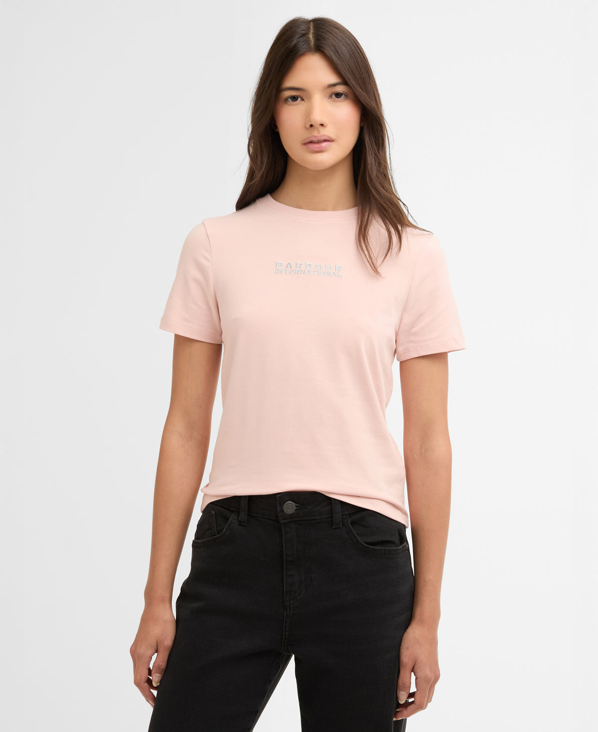 Woman wearing a light pink t-shirt with a barbour logo on a white background