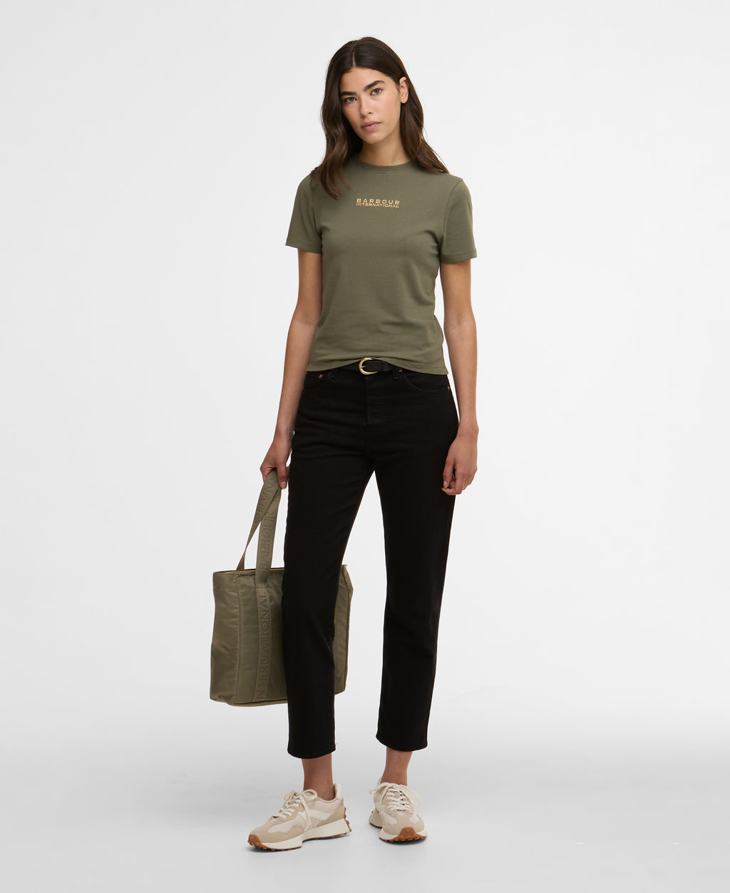 Woman wearing a green t-shirt and black pants, holding a green tote bag on a white background