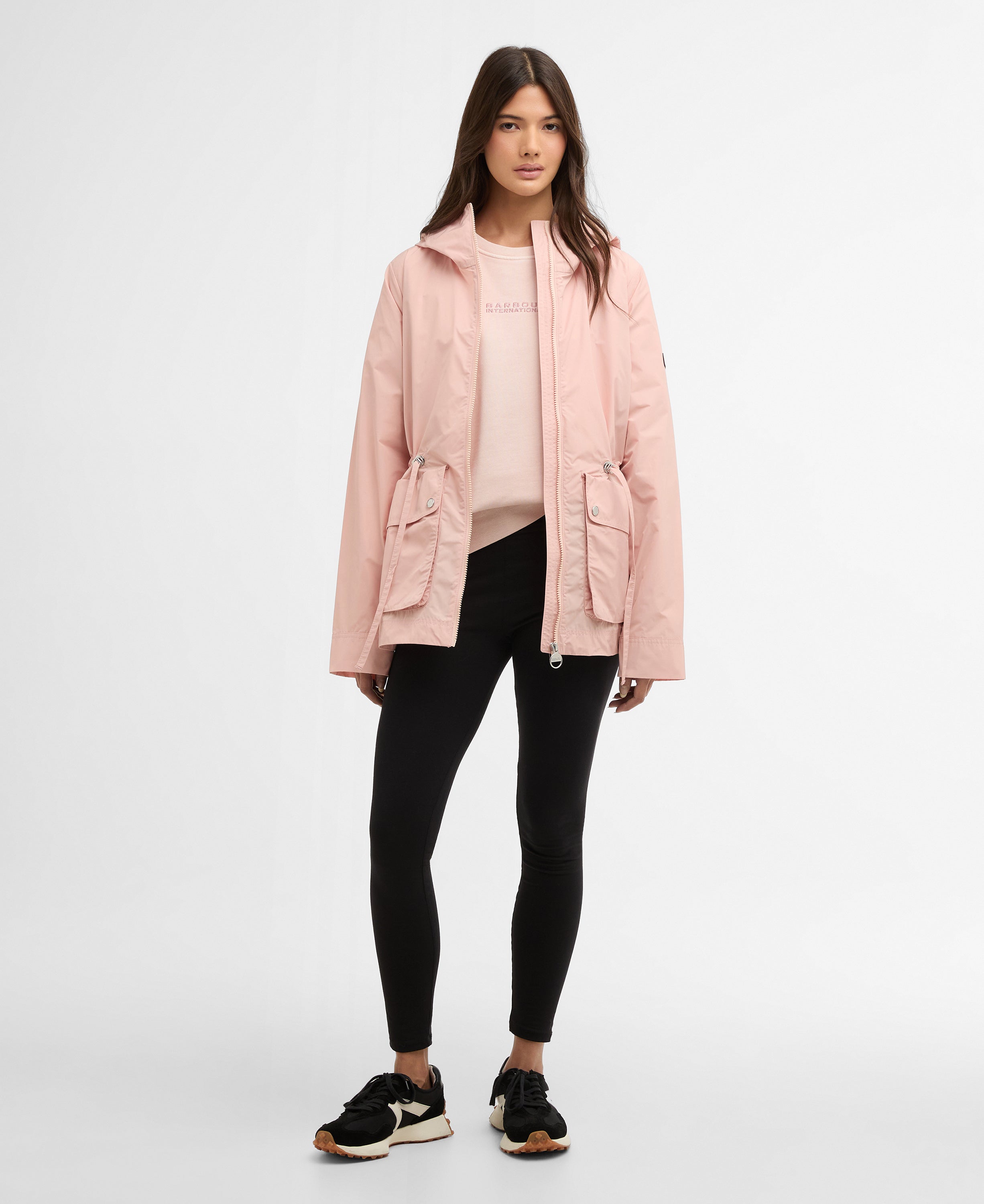 Woman wearing a pink jacket, black leggings, and black sneakers on a white background