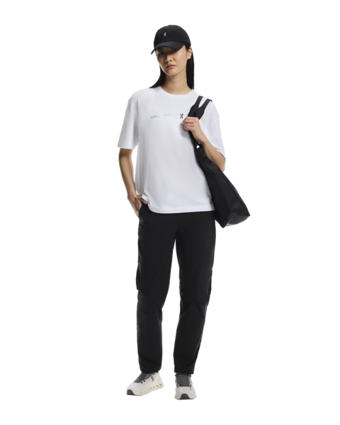 Person wearing a white t-shirt, black pants, and a black cap, holding a black bag on a white background