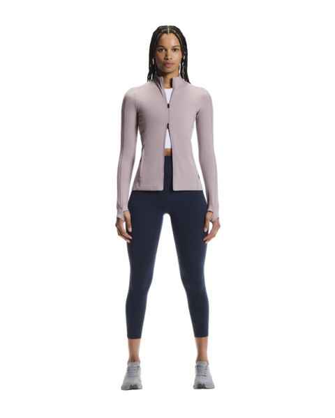 Woman wearing a light pink long-sleeve athletic jacket and dark blue leggings on a white background