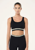 Woman wearing a black sports bra and leggings with visible branding on a beige background