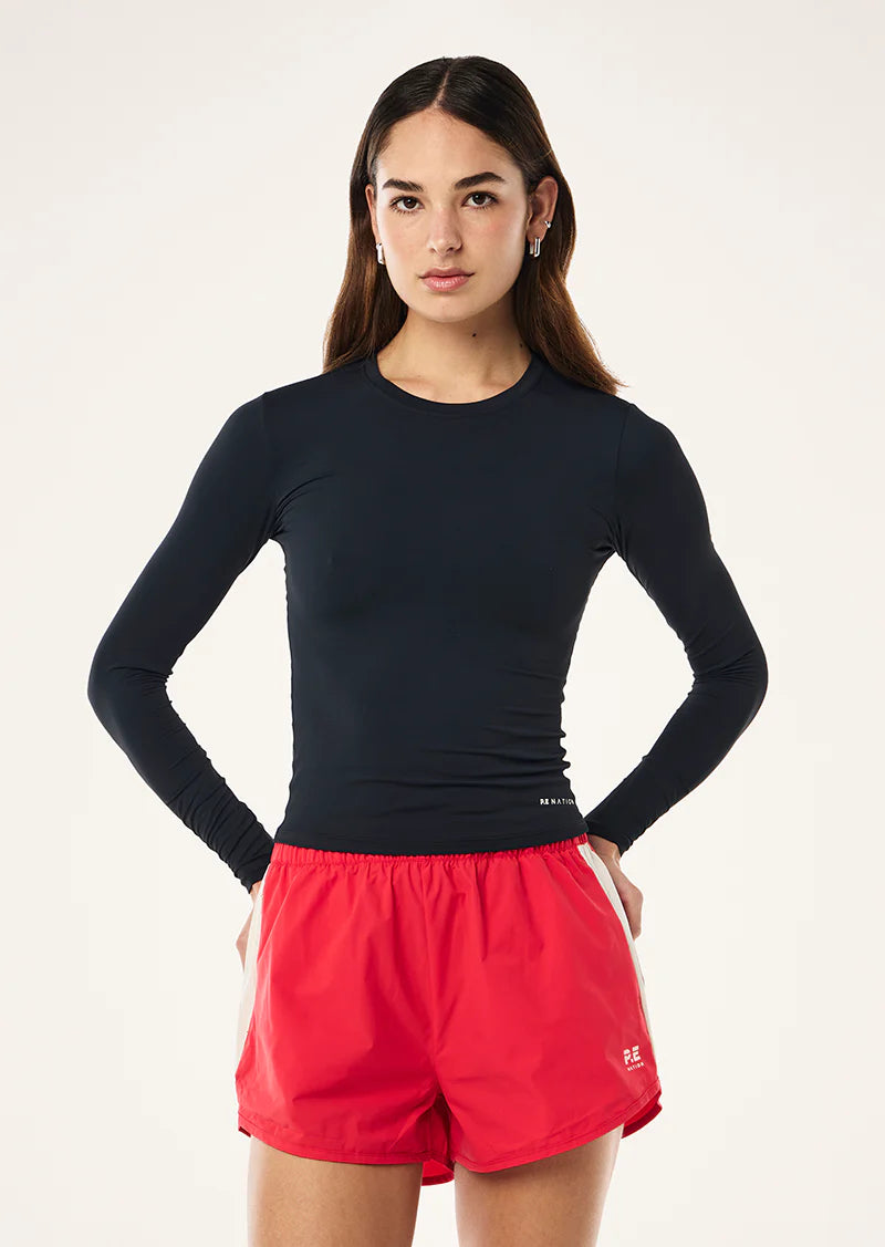 Woman wearing a navy blue long-sleeve top and red shorts on a white background