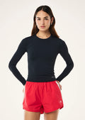 Woman wearing a navy blue long-sleeve top and red shorts on a white background