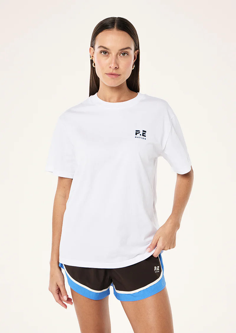 Woman wearing a white t-shirt with a logo and black shorts with blue accents on a white background