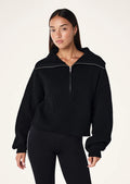 A woman wearing a black zip neck knit sweater with long sleeves, from the brand P.E Nation.