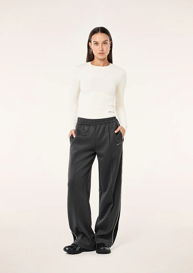 Person wearing a white sweater and black pants on a light pink background
