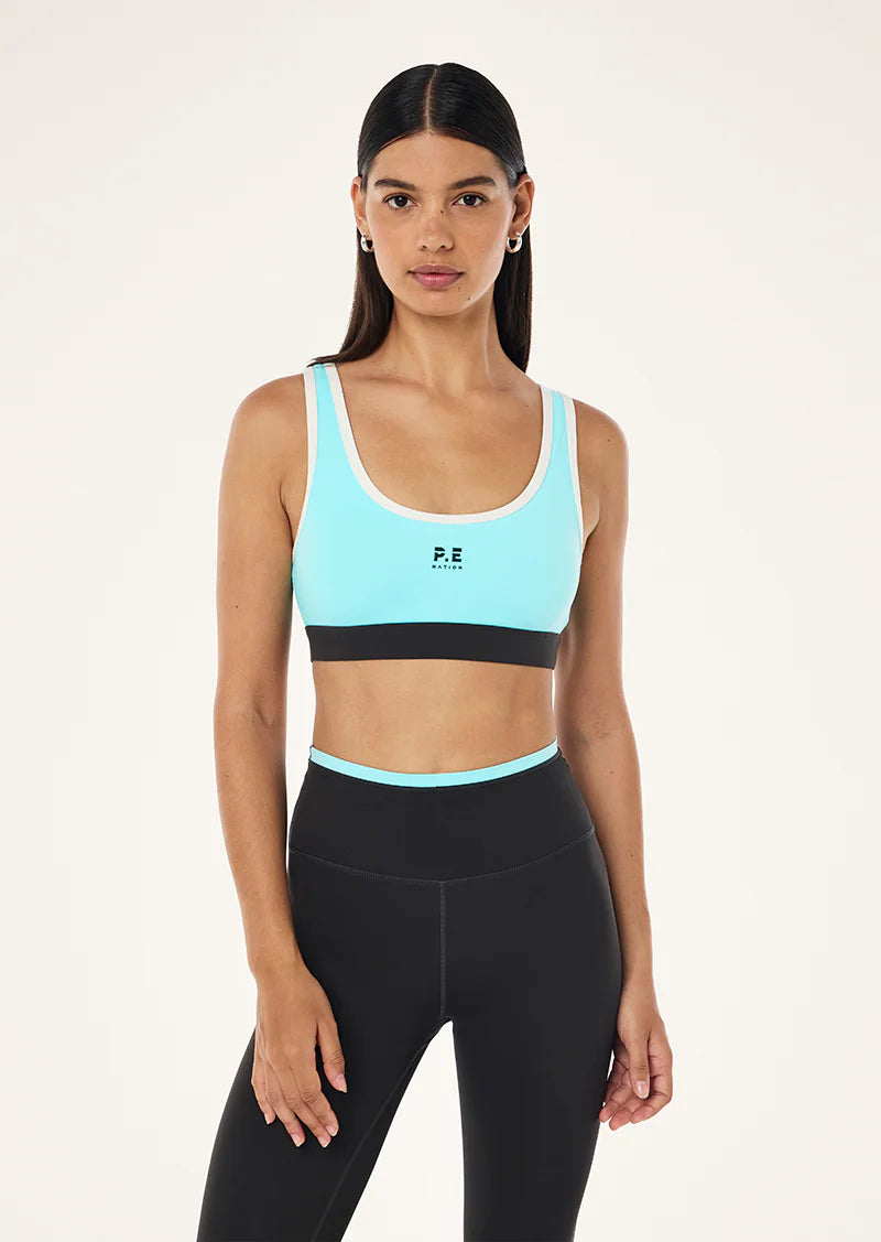 Woman wearing a light blue sports bra and black leggings on a white background