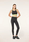 Woman wearing a grey sports bra and leggings with neon green accents on a white background
