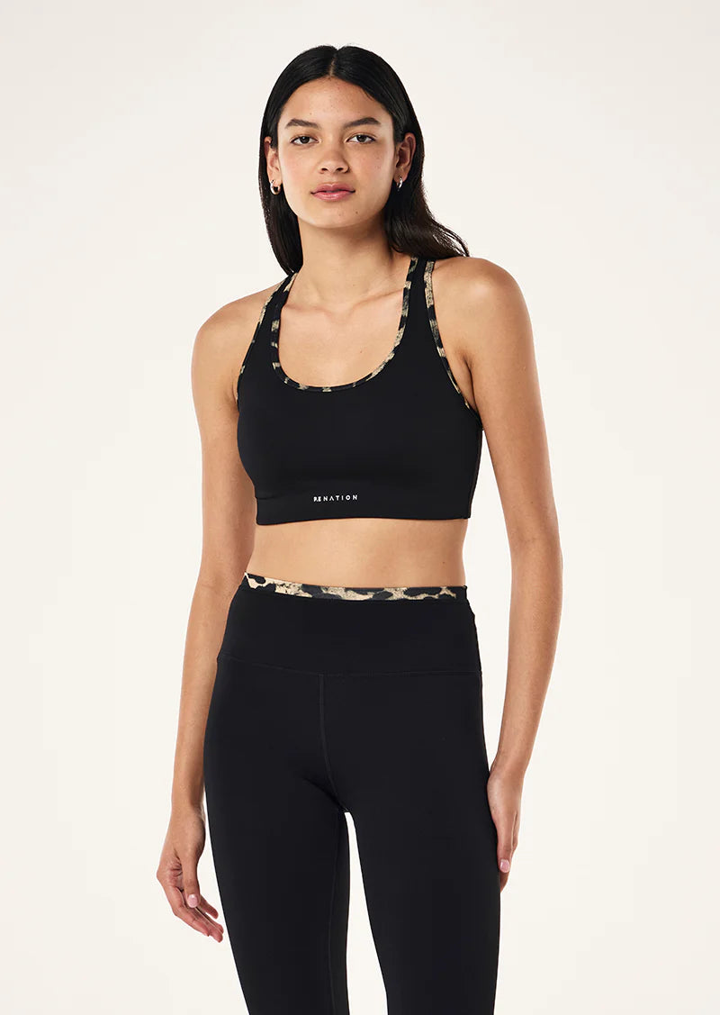 Woman wearing a black sports bra and leggings with a leopard print waistband on a white background