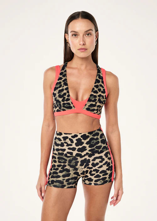 Woman wearing a leopard print sports bra and shorts with pink accents on a white background