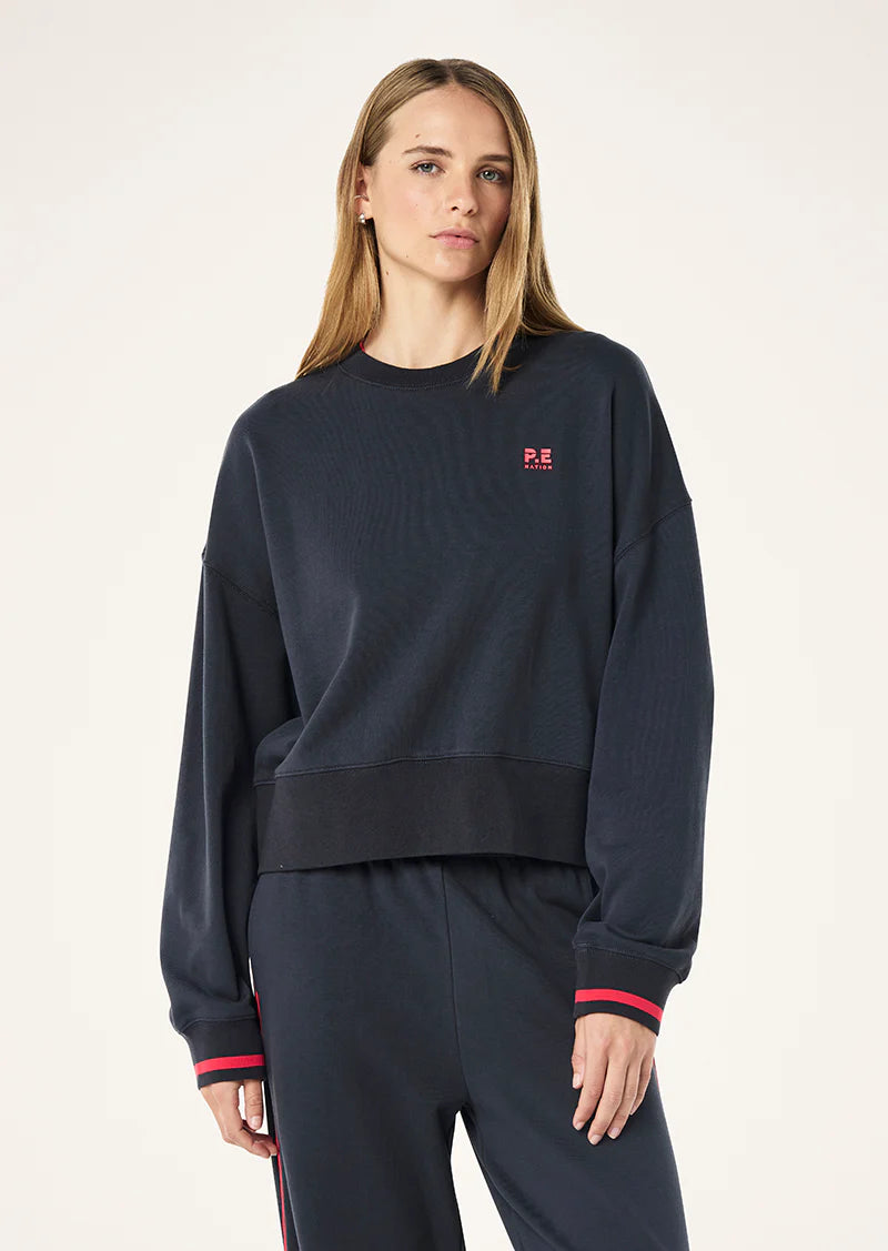 Person wearing a navy blue sweatshirt with a small red logo on a white background