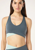 Woman wearing a gray and light blue sports bra and leggings on a white background