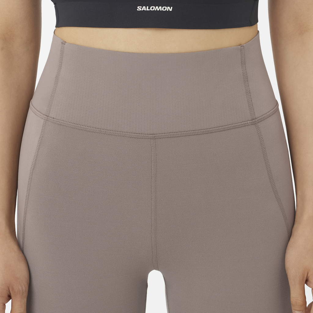 Person wearing brown leggings with a black sports bra featuring 'Salomon' branding.