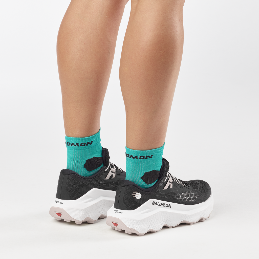 Person wearing teal socks with 'Salomon' branding and black athletic shoes on a white background