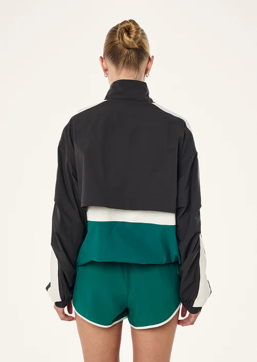Person wearing a black jacket with white accents and green shorts on a white background