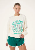 Person wearing a cream sweatshirt with green text and green shorts on a white background