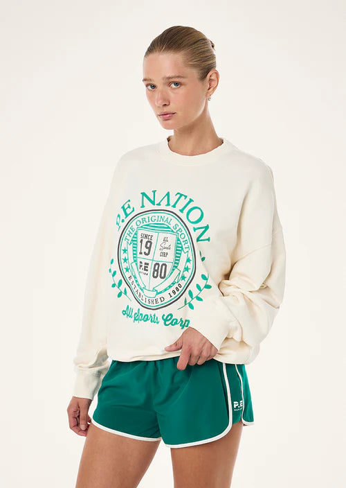 Woman wearing a cream sweatshirt with green text and green shorts on a white background