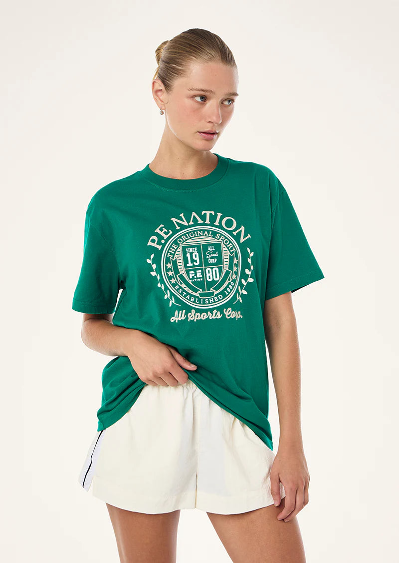 Woman wearing a green t-shirt with a logo and white shorts on a white background
