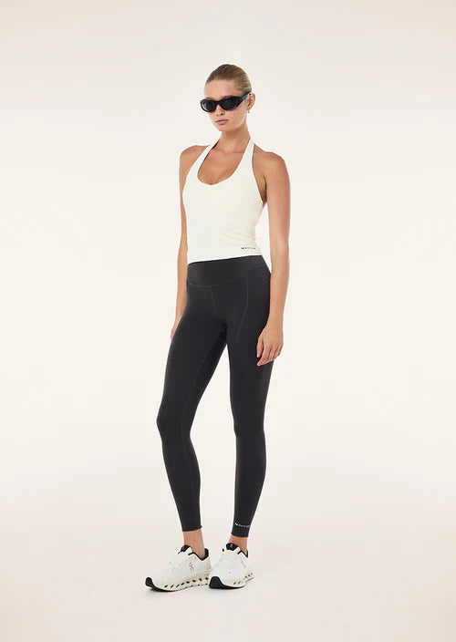 Woman wearing a white tank top and black leggings on a light background