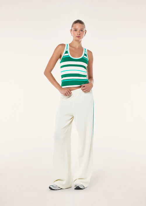 Woman wearing a green and white striped tank top and white pants on a white background