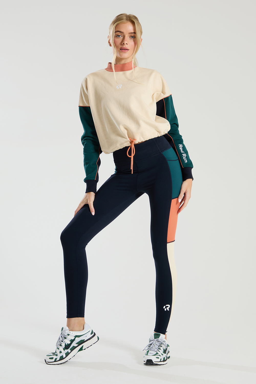 Woman wearing a beige and green  red run long-sleeve top with black leggings on a white background