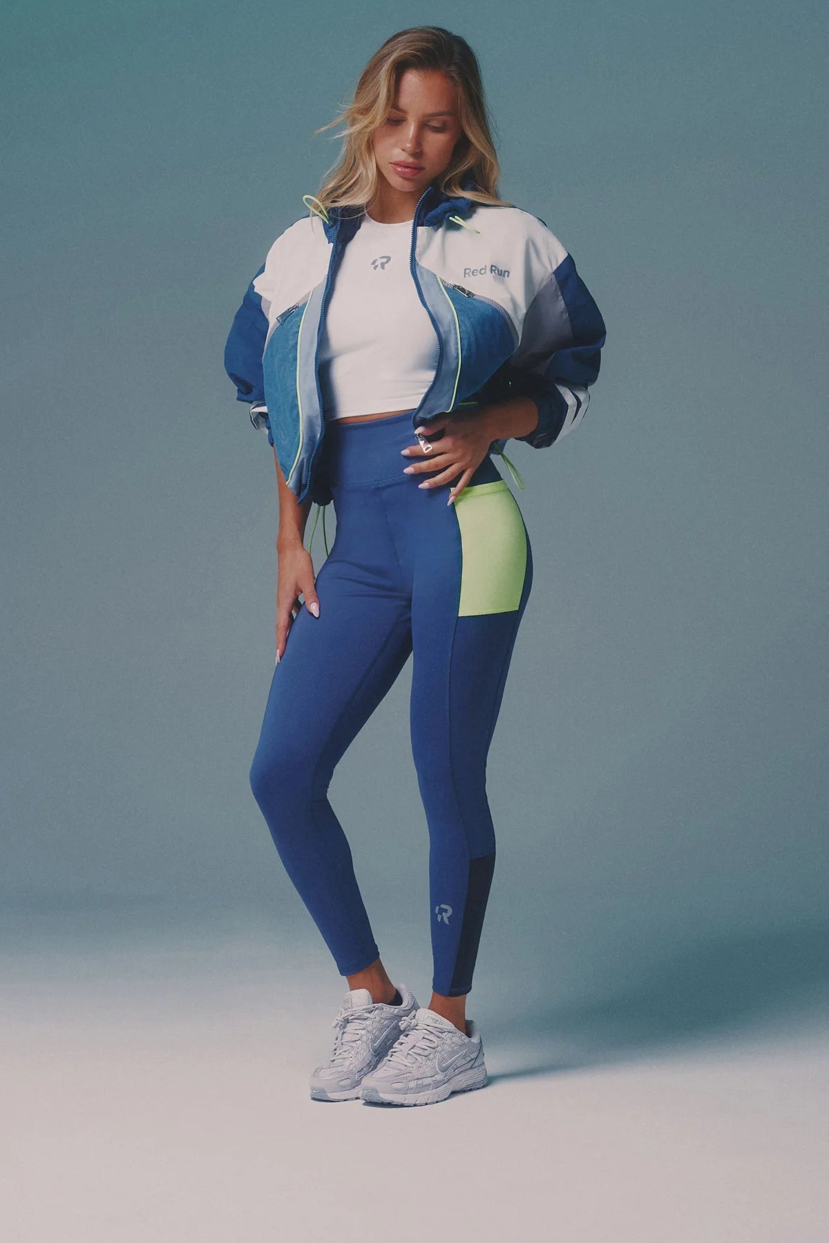 Woman wearing a blue and white athletic outfit with a green accent on a gray background