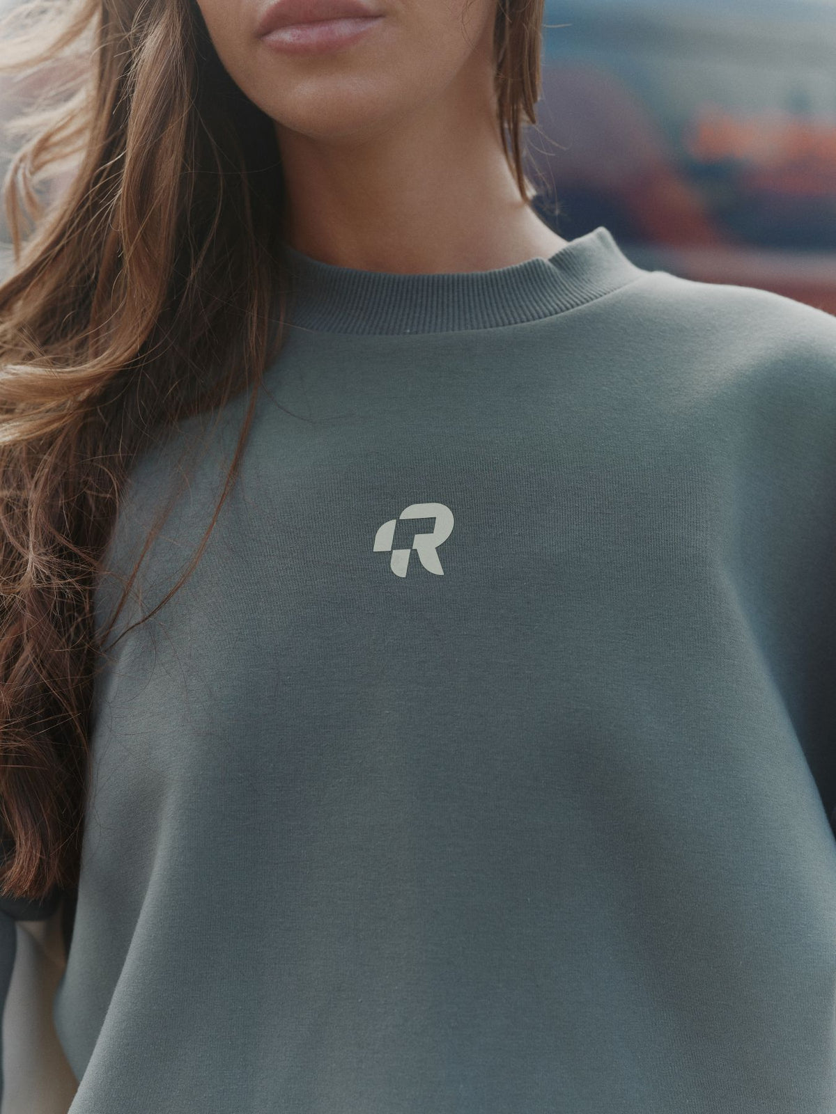 Person wearing a green sweater with a logo, blurred background